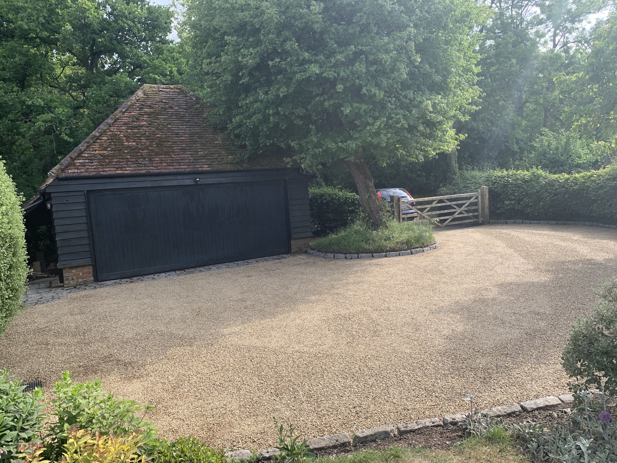 A wide golden gravel drive in front of a black timber garage