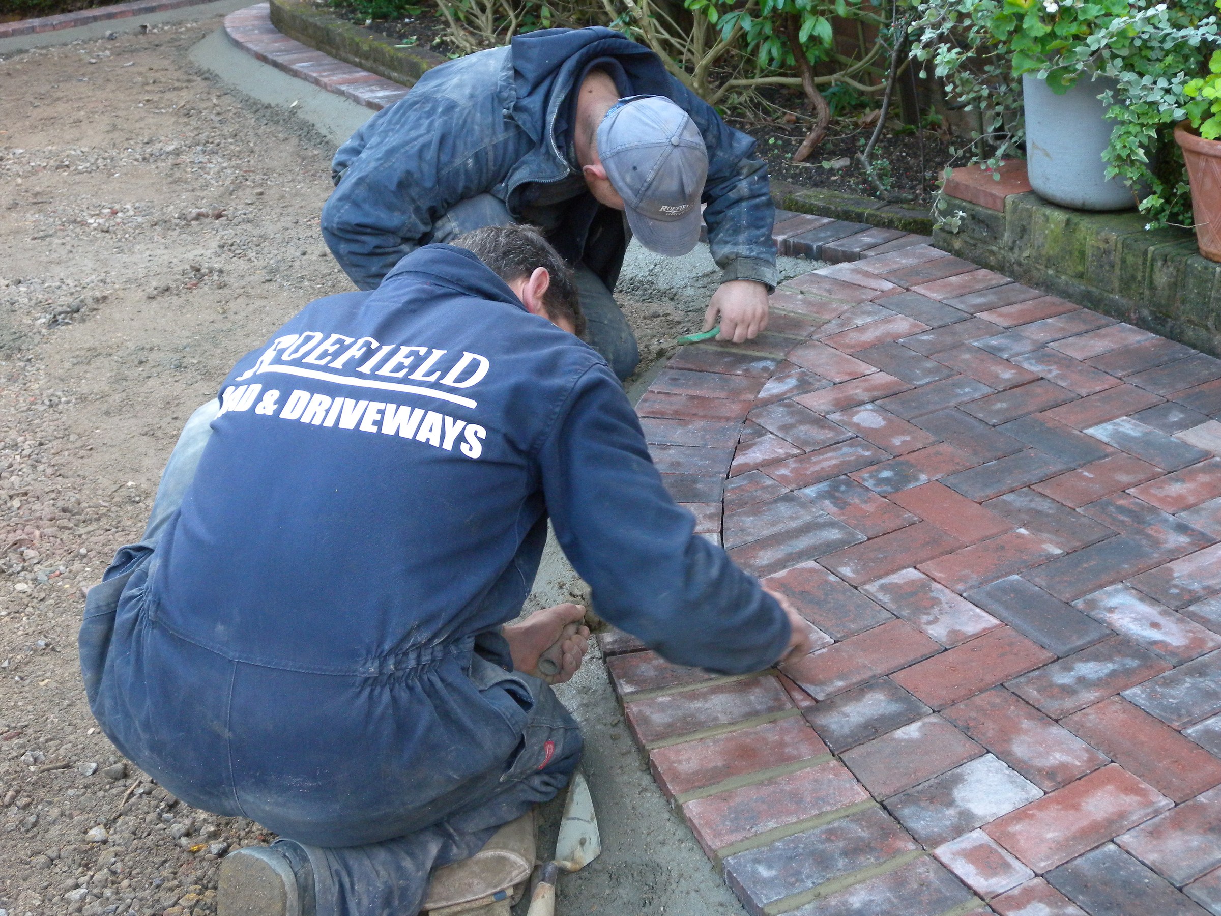 A Roefield paver in branded overalls laying red brick paving in a herringbone pattern