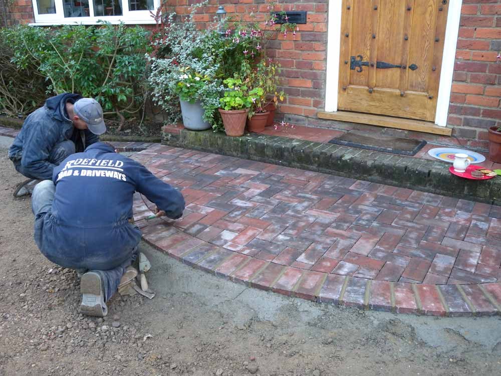 Two of our team laying curved brick paving at an oak front door
