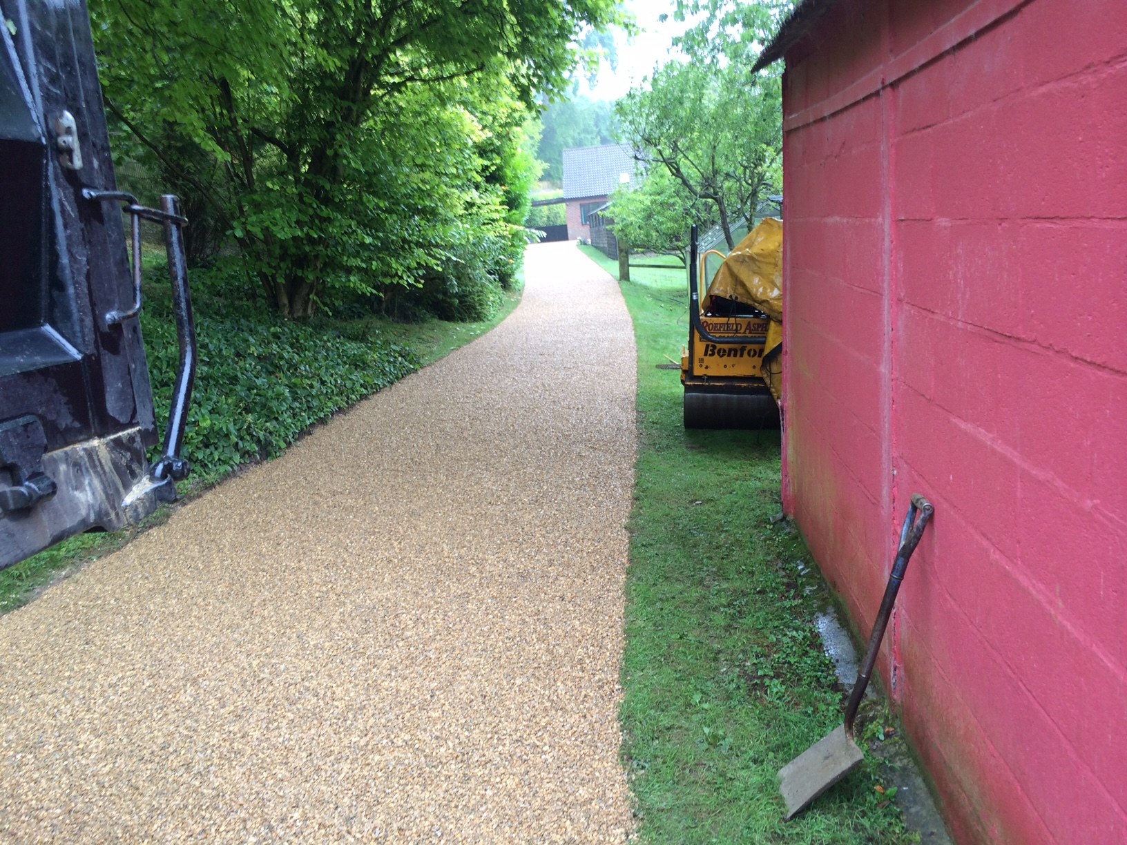 A fresh golden gravel path beside a pink wall, a roller behind