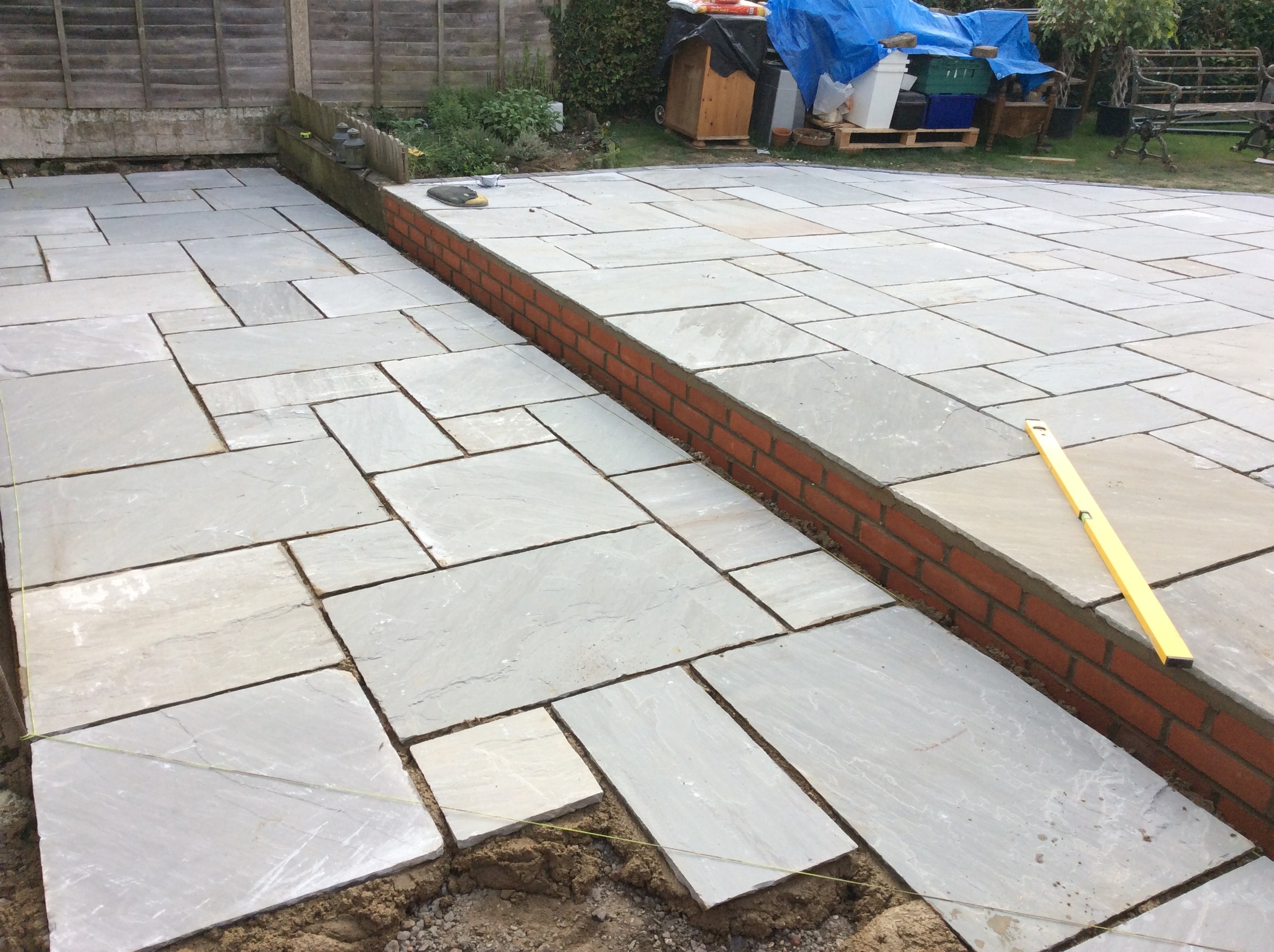 A new grey sandstone patio being laid beside a brick retaining wall, a spirit level on the slabs