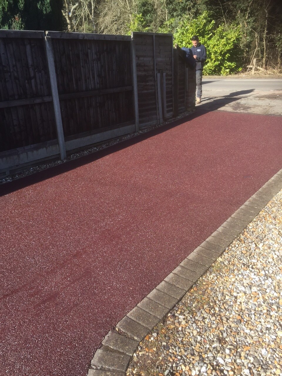 A red tarmac path with a block kerb beside a fence