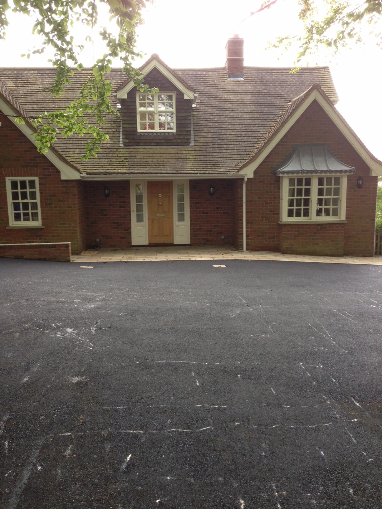 A black tarmac drive in front of a dormer cottage