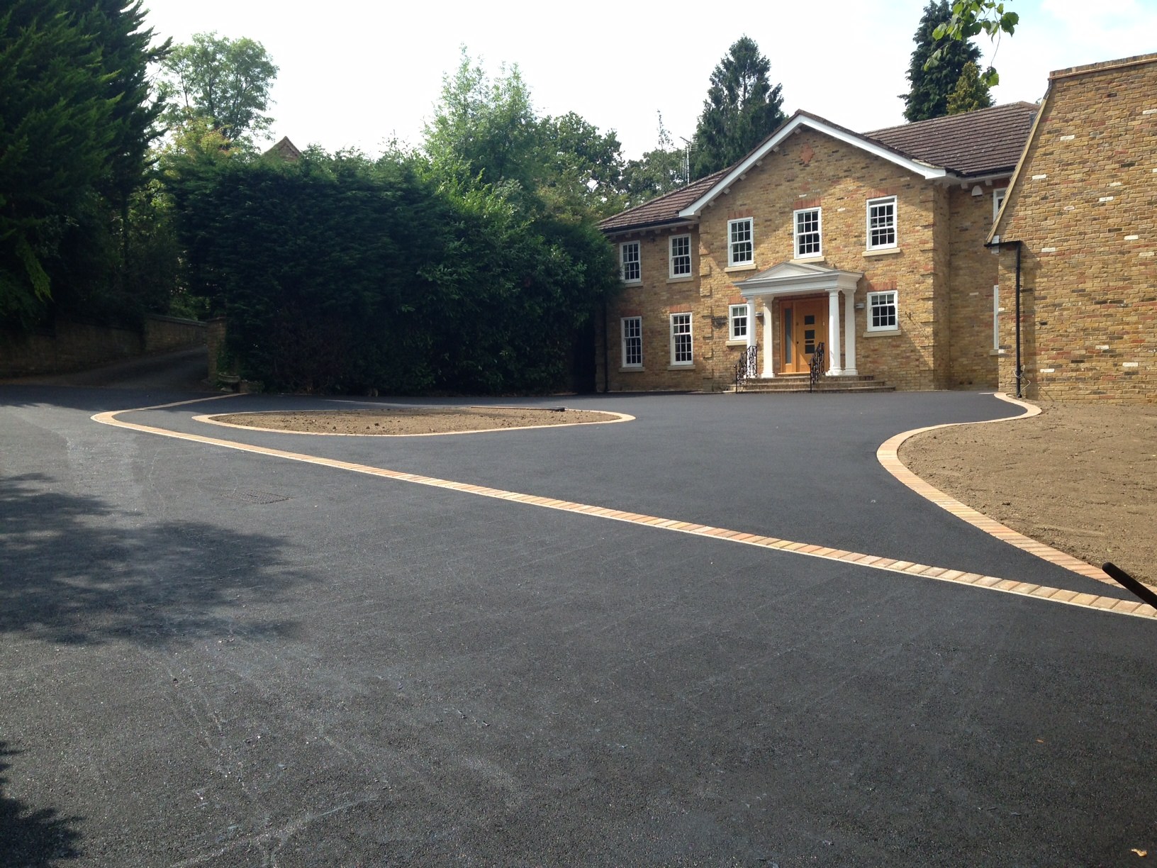 A large tarmac turning circle with buff kerb edging in front of a stone house