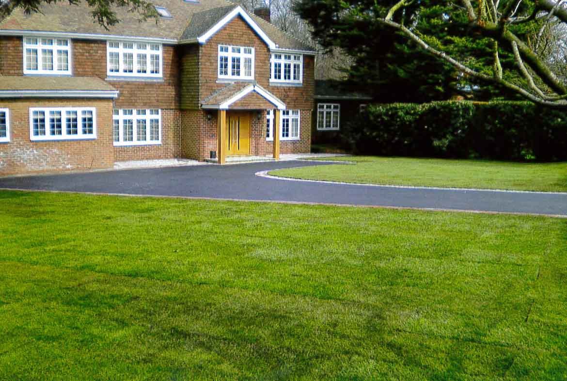 A sweeping new tarmac drive with block edging across a lawn to a large brick house